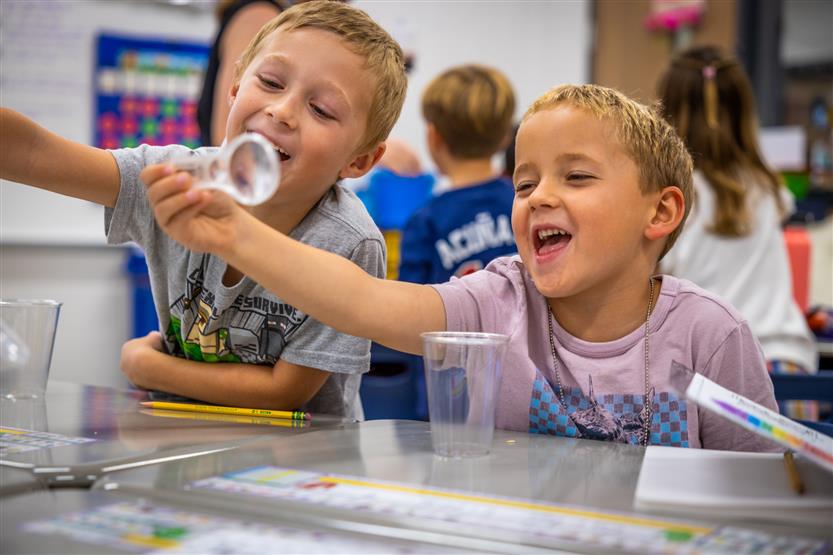 Two boys laugh while using a magnifying glass